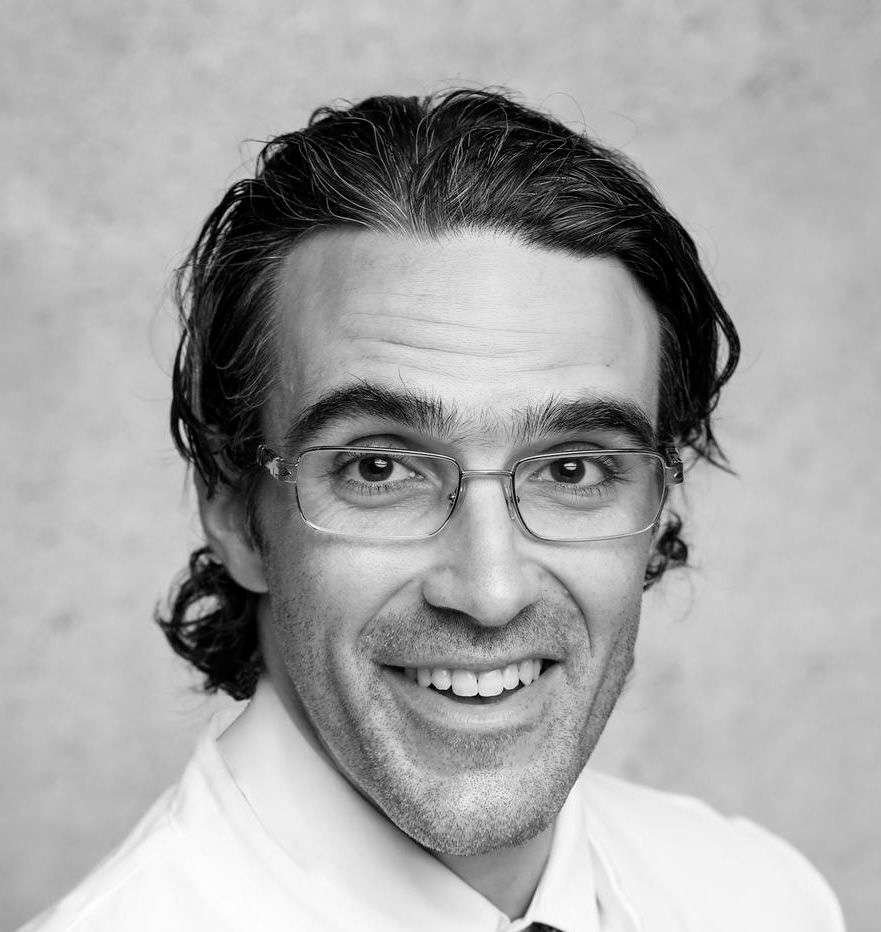 Smiling man with glasses in black and white portrait.